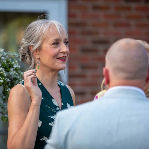 Candid event photography in Cheshire featuring a woman in a green floral dress talking to guests at a garden party.